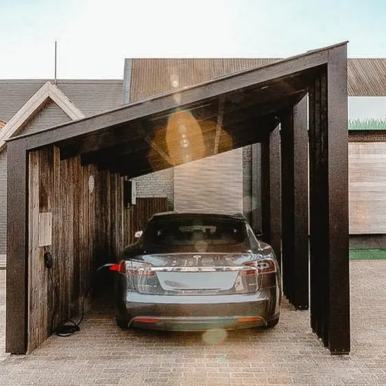 Voiture électrique garée sous un abri d’auto moderne en bois sombre avec toit incliné, en train de se recharger.