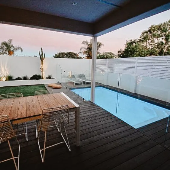 Clôture de piscine en verre élégante et sécurisée entourant une piscine moderne, avec un espace de détente à proximité.