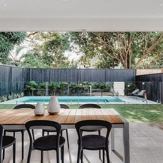 Piscine moderne avec une élégante clôture en bois, entourée de verdure et d'une maison contemporaine en arrière-plan.