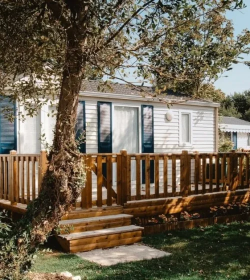 Une maison mobile confortable entourée de verdure, avec un espace extérieur en bois qui améliore son attrait accueillant.