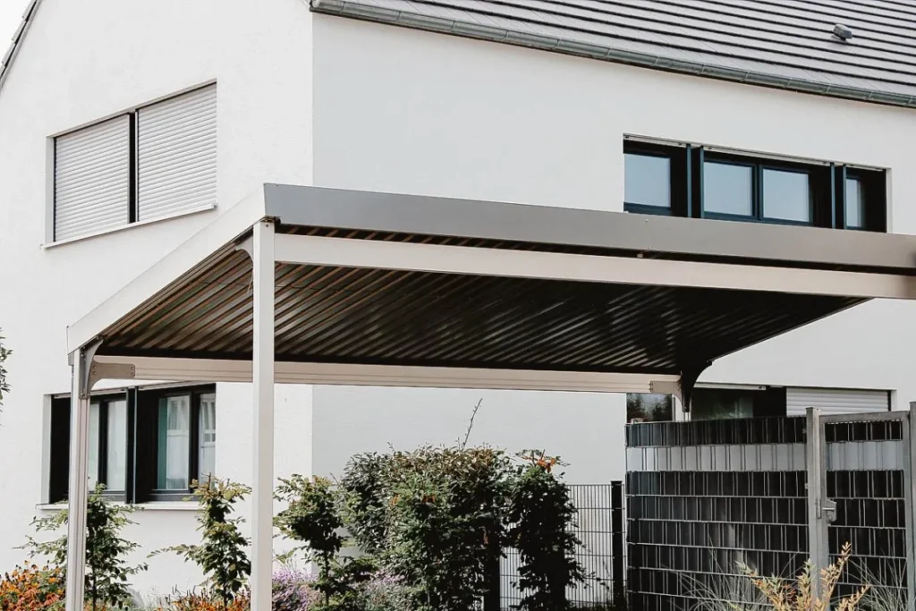 Abri d’auto moderne en métal avec toit en pente, situé devant une maison contemporaine aux murs blancs.