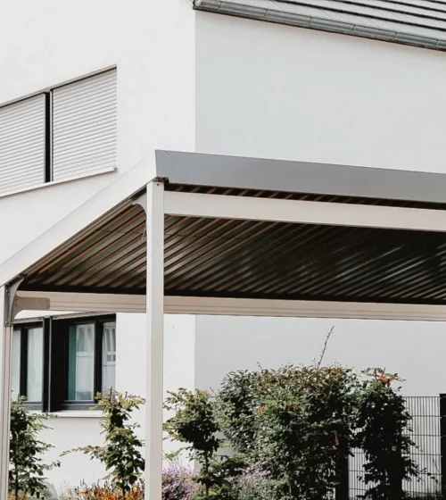 Abri d’auto moderne en métal avec toit en pente, situé devant une maison contemporaine aux murs blancs.