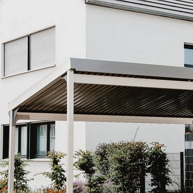 Abri d’auto moderne en métal avec toit en pente, situé devant une maison contemporaine aux murs blancs.