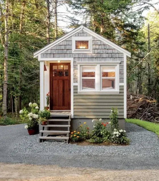 Charming tiny house with a small wooden porch, surrounded by flowering plants, set in a peaceful forest.