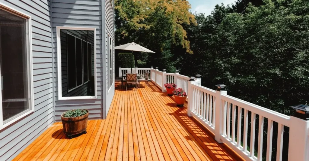 Terrasse en bois avec balustrades blanches, sièges extérieurs et plantes en pot.