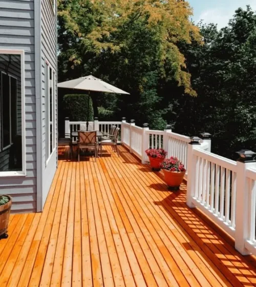 Terrasse en bois avec balustrades blanches, sièges extérieurs et plantes en pot.