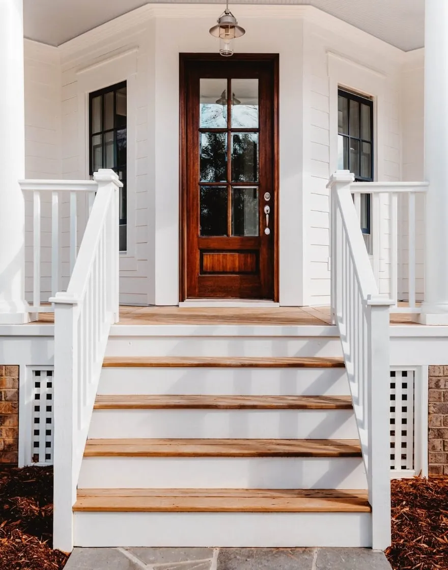 Escalier en bois menant à une porte d'entrée élégante, avec une rampe blanche, sur une terrasse solide et bien conçue.