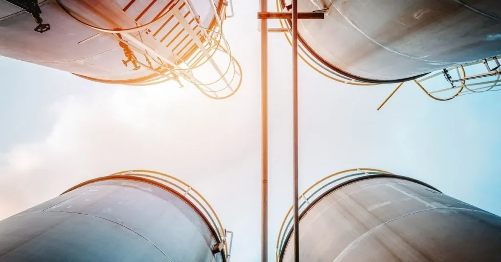 Silos agricoles en métal vus depuis le sol, avec un ciel lumineux en arrière-plan.