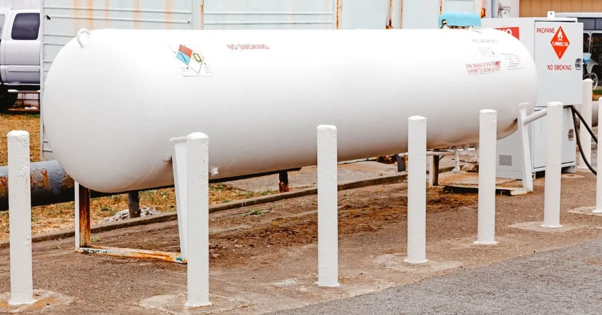 Large white propane gas tank secured with bollards on a stable surface, used for commercial or industrial purposes.