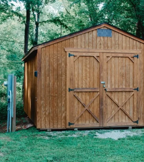 Cabanon de jardin en bois avec de grandes portes doubles, situé au milieu d'une forêt verdoyante.