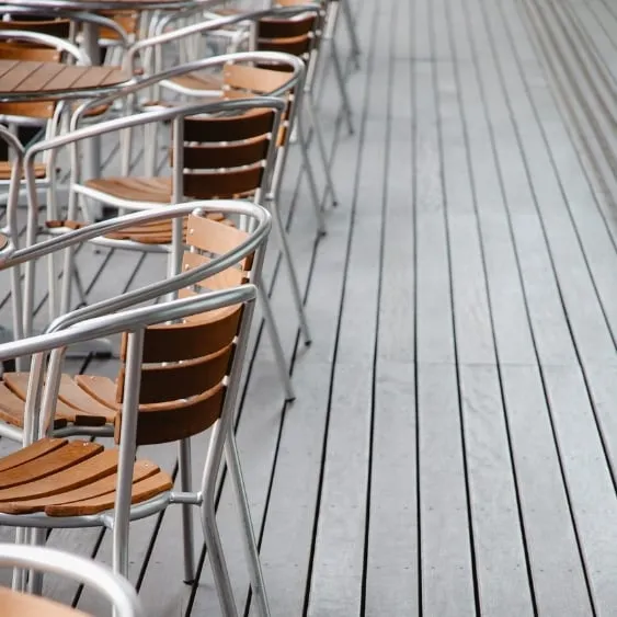 Rows of modern outdoor chairs with wooden seats and metal frames, arranged on a sleek wooden deck.