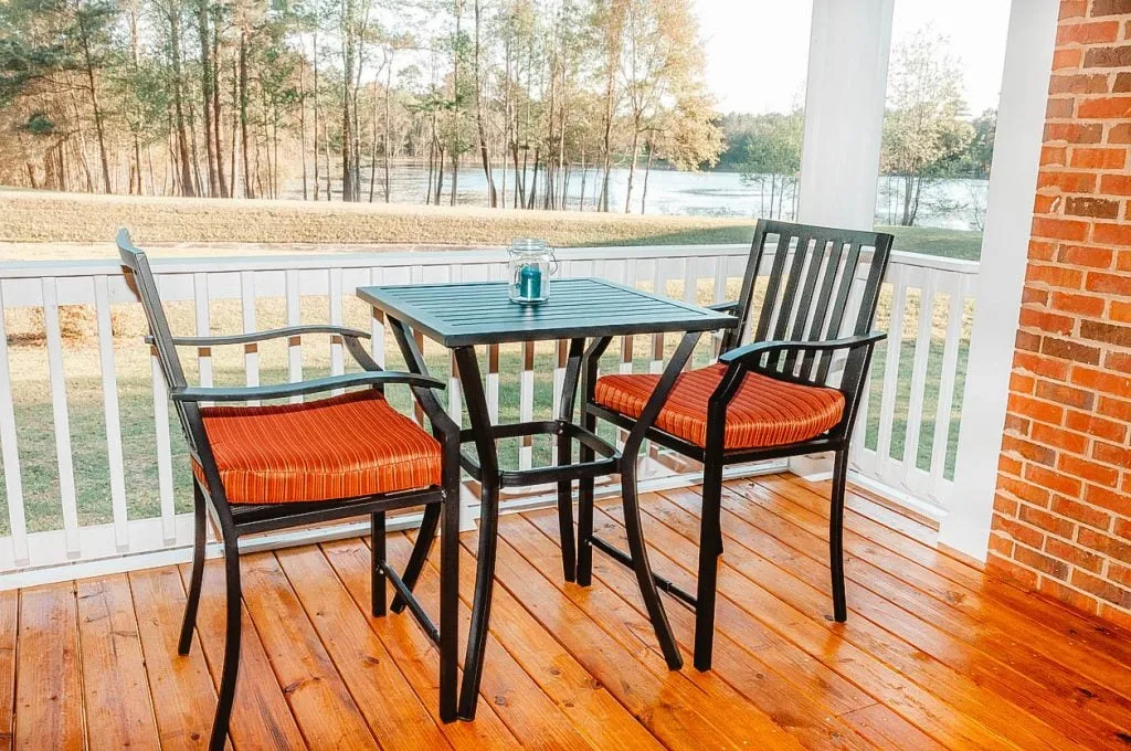 A dining setup on a deck featuring a table and chairs, overlooking a lush landscape and a body of water in the background.