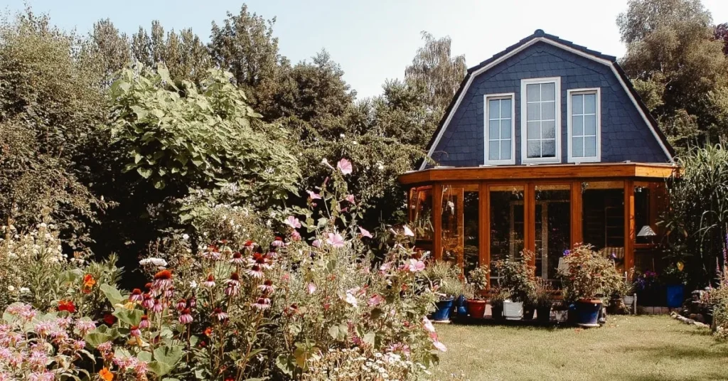 Une véranda en bois avec de grandes fenêtres vitrées, entourée d'un jardin fleuri en pleine nature.