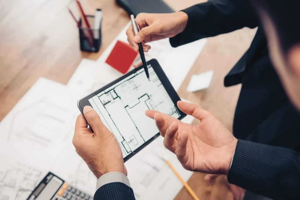 Des professionnels examinant des plans de construction sur une tablette, entourés de documents de conception, illustrant la planification dans le secteur de la construction.