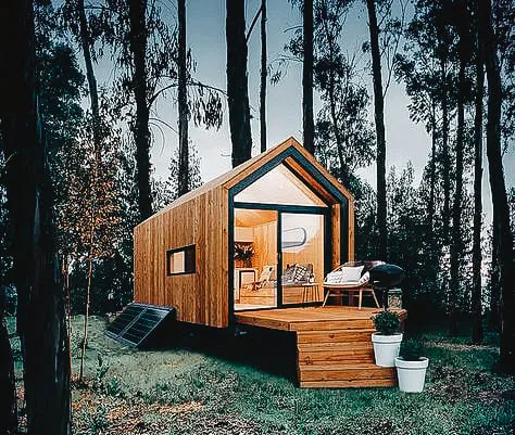 Modern tiny house in the woods with a wooden deck and large windows.