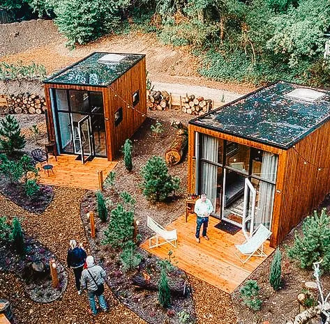 Mini-maisons modernes avec extérieurs en bois dans un cadre forestier, avec petites terrasses et aménagement paysager minimaliste.