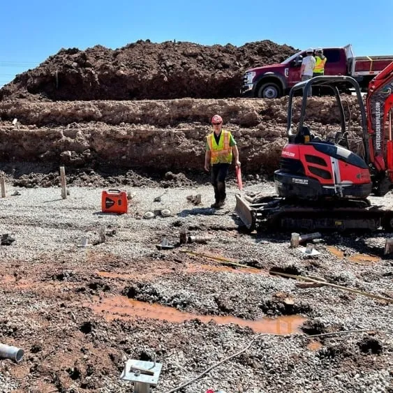 Construction workers at a site with heavy machinery and gravel, preparing the foundation for a new building, ensuring a stable base.