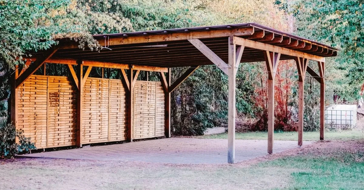 Carport en bois avec un toit solide et des panneaux de confidentialité, situé dans un jardin verdoyant et boisé.