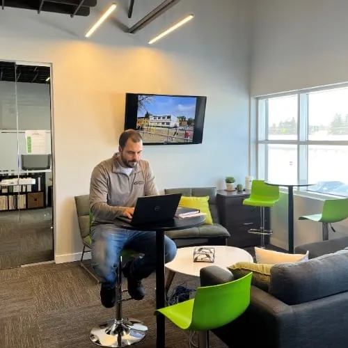 Personne travaillant sur un ordinateur portable dans un salon de bureau moderne, représentant un environnement de travail dynamique et confortable.