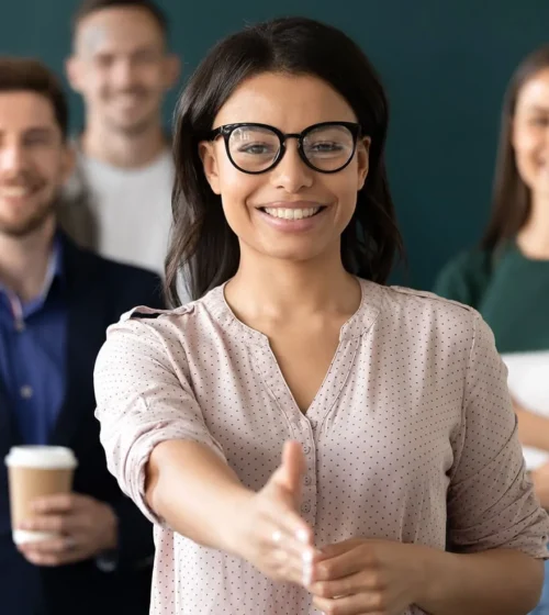 Femme souriante tendant la main pour une poignée de main, représentant une approche accueillante et professionnelle.