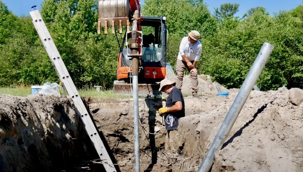 Travailleurs installant des pieux vissés à l'aide d'un excavateur sur un chantier de construction, illustrant les techniques modernes de fondation.