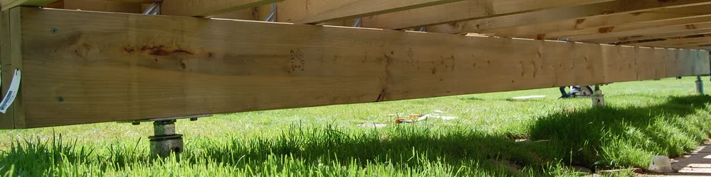 Vue latérale d'une structure en bois soutenue par des pieux vissés, avec de l'herbe verte en dessous.