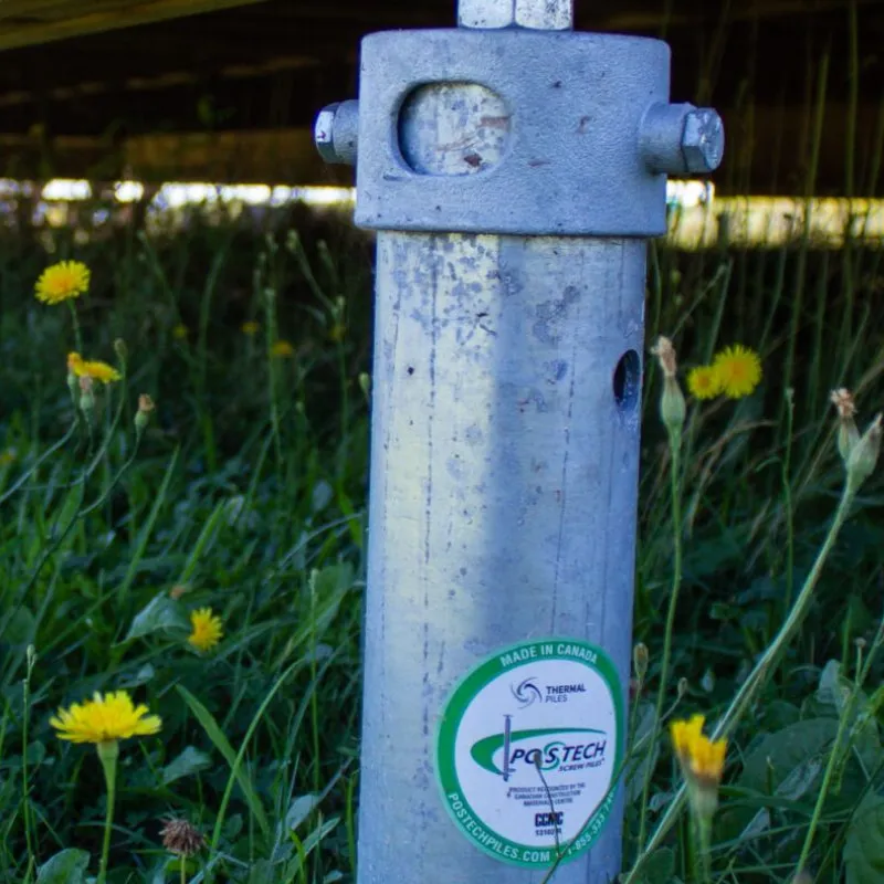 Pieu vissé Postech installé sous une structure, visible dans un environnement herbeux.