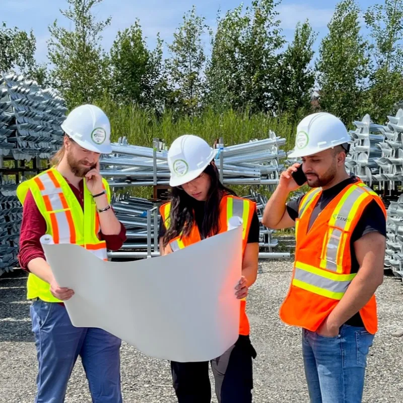 Trois professionnels de la construction examinant des plans sur un site, portant des gilets de sécurité et des casques de protection