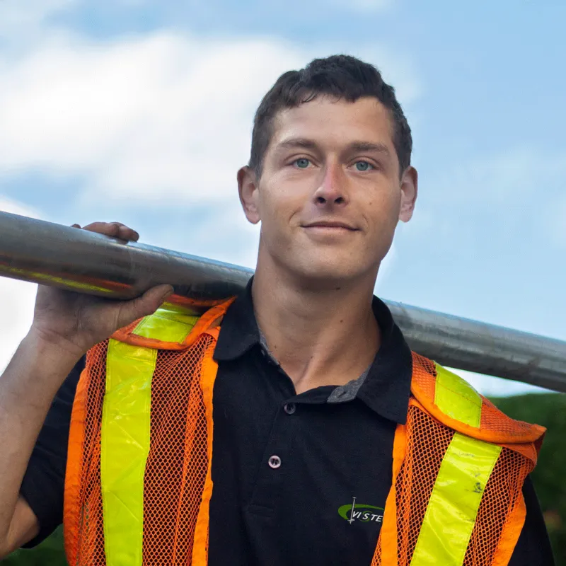 Technicien Vistech portant un pieu vissé sur l'épaule, vêtu d'un gilet de sécurité orange