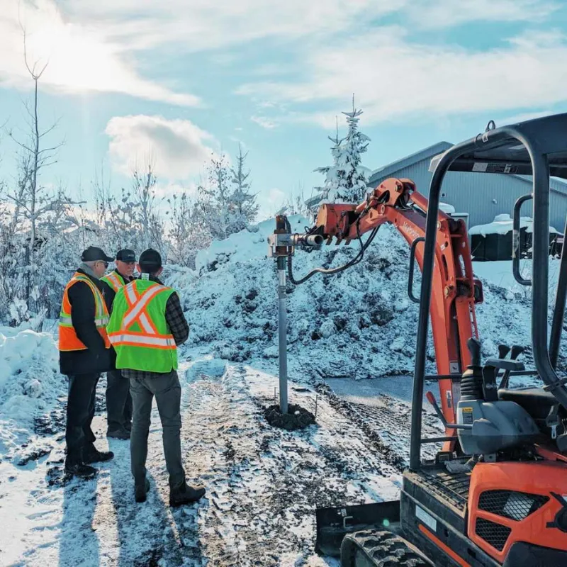 Installation de pieux vissés Vistech en hiver avec une machine de chantier et trois techniciens sur site