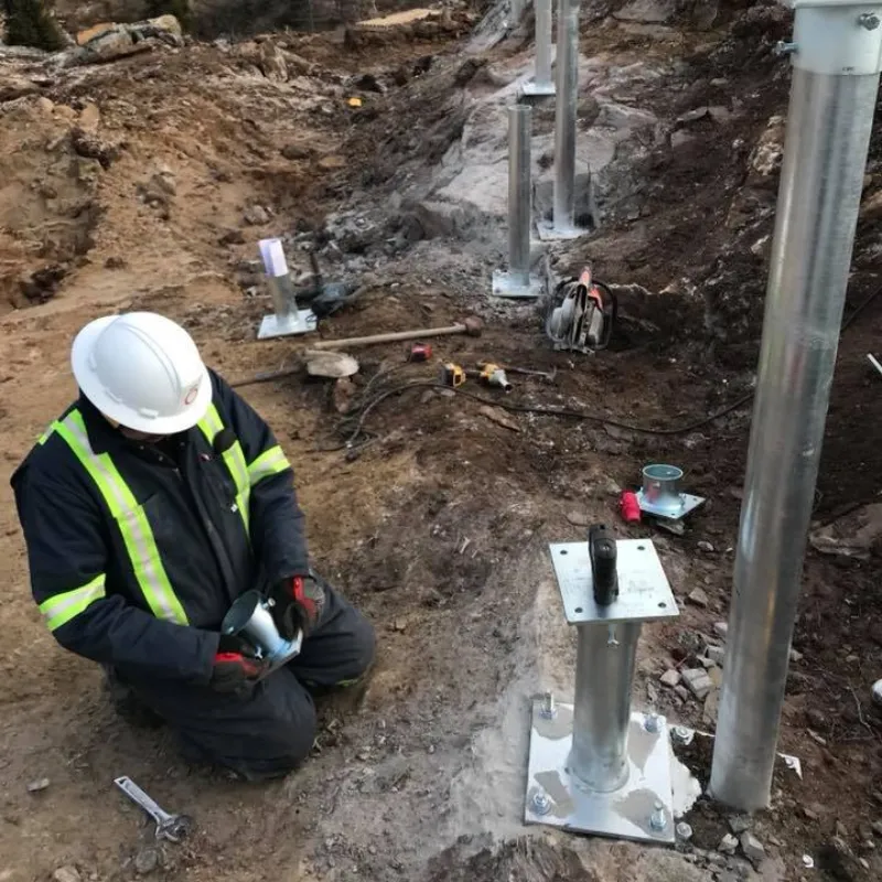 Travailleur installant des pieux vissés dans un terrain rocheux.