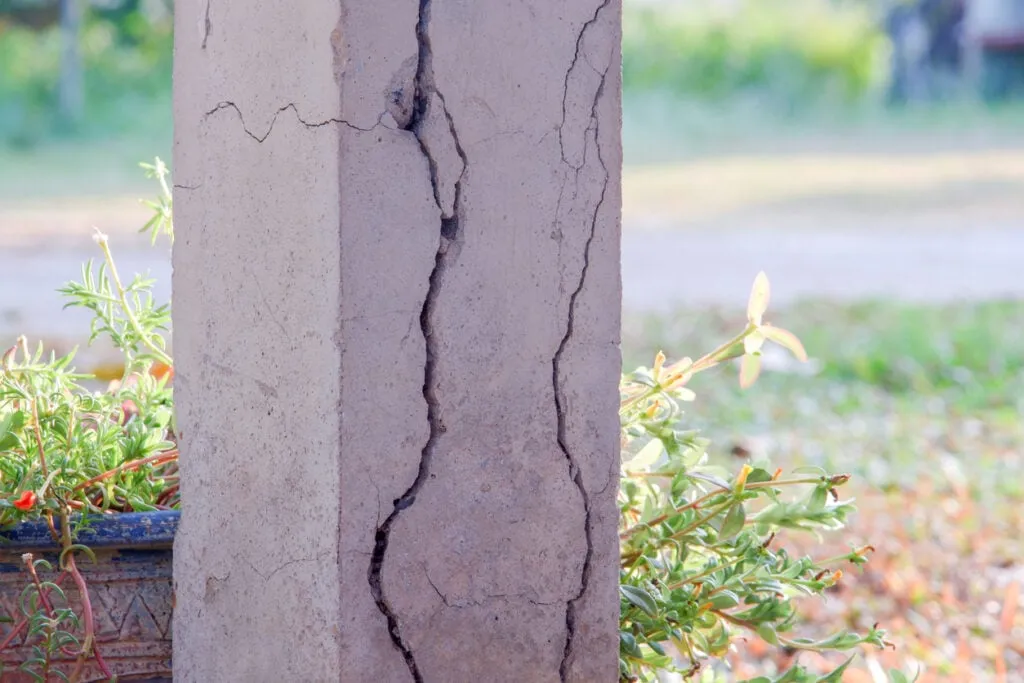 Pilier en béton présentant une fissure importante, illustrant les dangers de fondations instables ou mal construites.